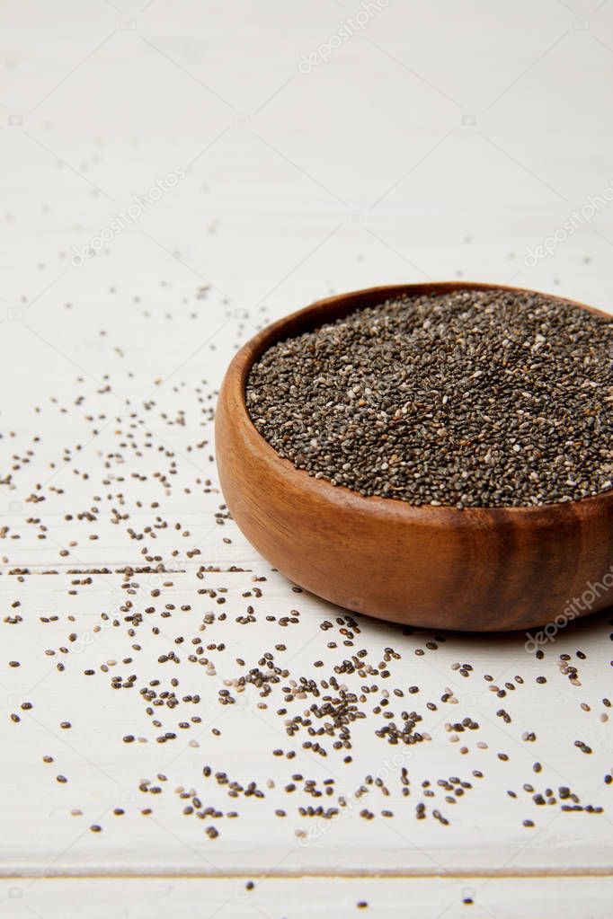 close up view of wooden bowl with chia seeds on white surface