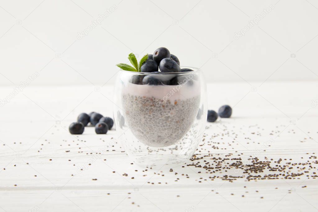close up view of sweet chia seed pudding with blueberries and mint on white wooden surface