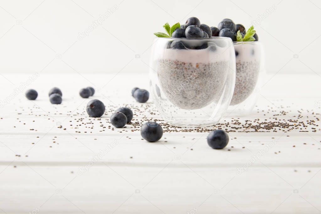 close up view of chia puddings with fresh blueberries and mint on white wooden tabletop