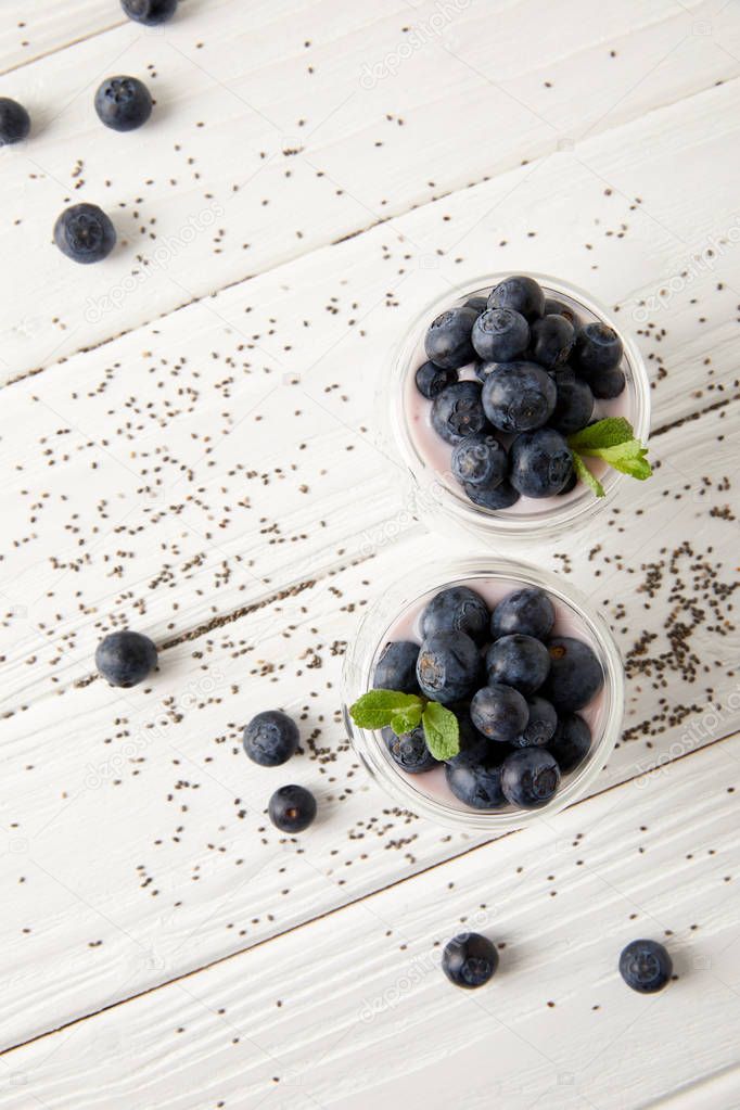 top view of arranged chia puddings with fresh blueberries and mint on white wooden surface