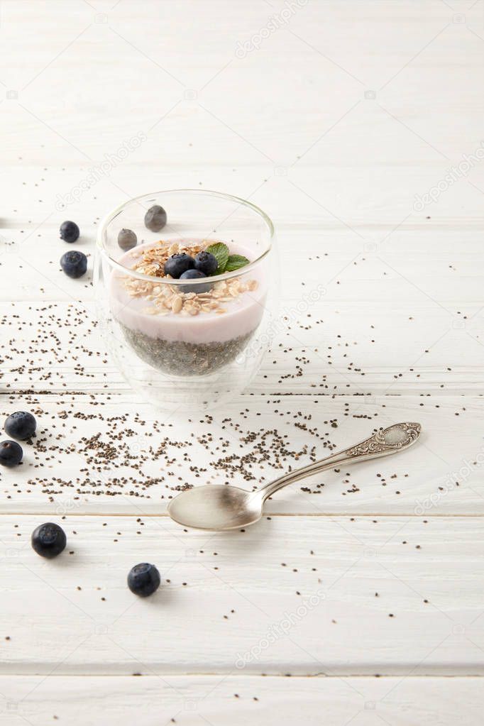 close up view of chia pudding dessert with blueberries and oatmeal on white wooden surface