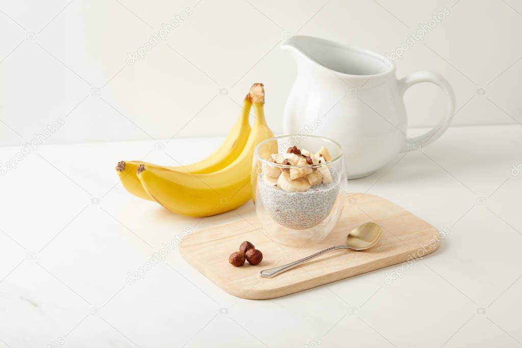 close up view of tasty chia seed pudding with bananas and hazelnuts on white tabletop
