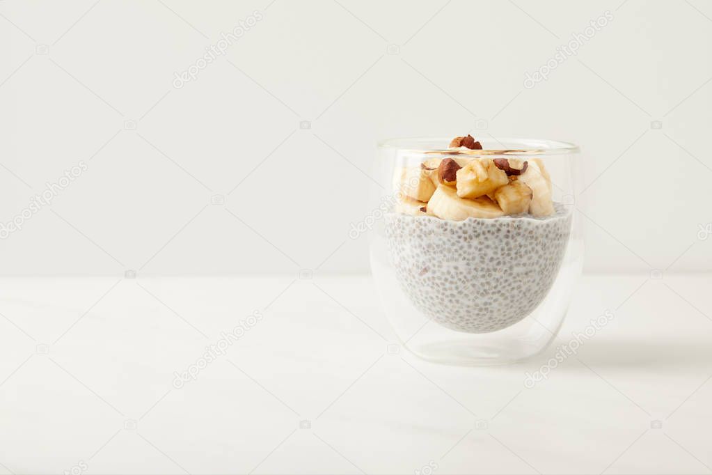 close up view of tasty chia seed pudding with pieces of banana and hazelnuts on white tabletop