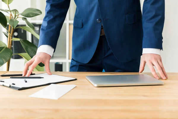 Vue partielle de l'homme d'affaires en costume sur le lieu de travail avec des documents et un ordinateur portable au bureau — Photo