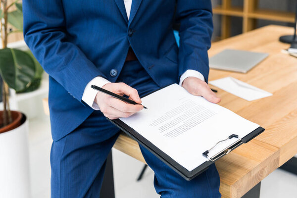 cropped shot of businessman with notepad and pen in hands at workplace in office
