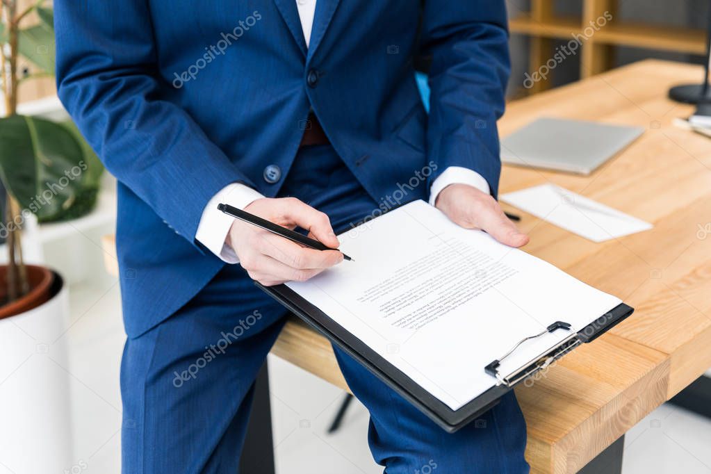 cropped shot of businessman with notepad and pen in hands at workplace in office