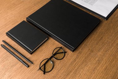 close up view of black notebooks, eyeglasses and stationery on wooden tabletop clipart