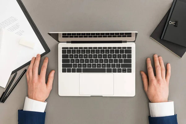 Tiro cortado de homem de negócios no local de trabalho com laptop, bloco de notas e cadernos — Fotografia de Stock