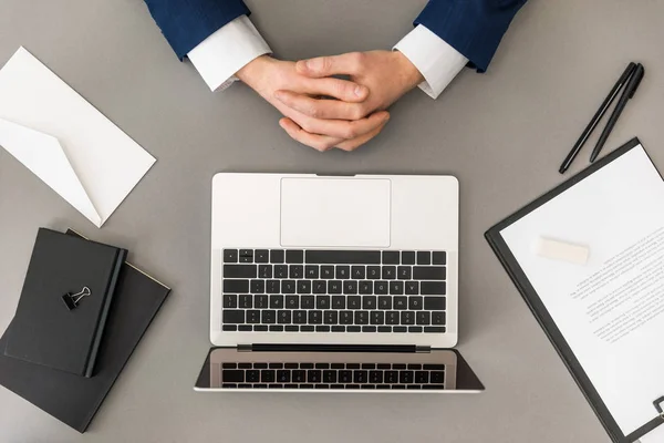 Обрезанный снимок бизнесмена с закрытыми руками на рабочем месте с ноутбуком, блокнотом и ноутбуком — стоковое фото