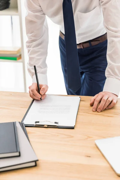 Gedeeltelijke weergave van zakenman ondertekenen papieren op werkplek op kantoor — Gratis stockfoto