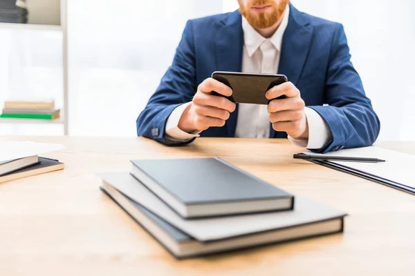 Vue partielle de l'homme d'affaires en costume à l'aide d'un smartphone sur le lieu de travail avec des ordinateurs portables au bureau — Photo gratuite