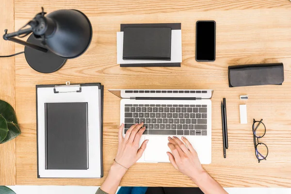 Vue partielle de la femme d'affaires tapant sur ordinateur portable au travail avec des lunettes et des documents — Photo