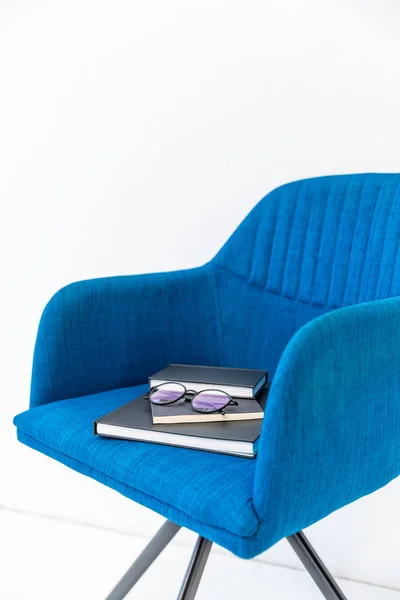 Close up view of pile of black notebooks and eyeglasses on blue chair on white backdrop — Stock Photo, Image