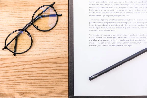 Top view of eyeglasses, pencil and notepad with documents on wooden surface — Free Stock Photo