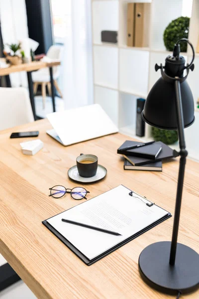 Close up view of cup of coffee, eyeglasses, documents and lamp at workplace in office — Stock Photo, Image