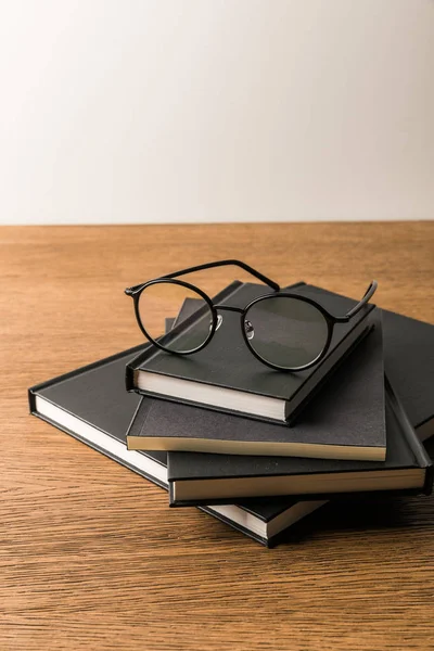 Close up view of pile of black notebooks and eyeglasses on wooden tabletop — Free Stock Photo