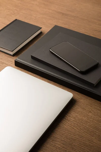 Close up view of laptop, pile of black notebooks and smartphone on wooden tabletop — Free Stock Photo