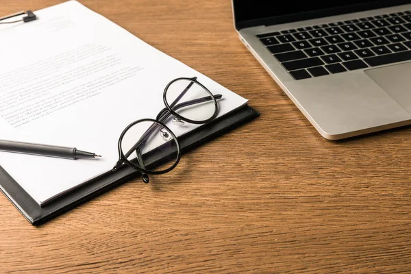 Close up view of eyeglasses, laptop and notepad with pen on wooden tabletop — Stock Photo, Image