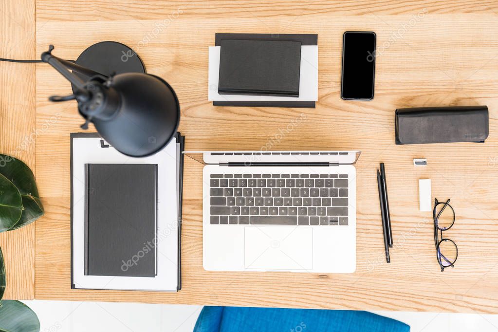 top view of arranged eyeglasses, laptop, notebooks and smartphone at workplace