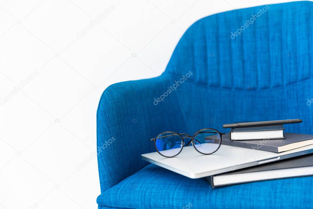 close up view of laptop, black notebooks and eyeglasses on blue chair on white background 