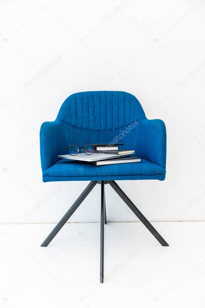 close up view of laptop, black notebooks and eyeglasses on blue chair on white backdrop