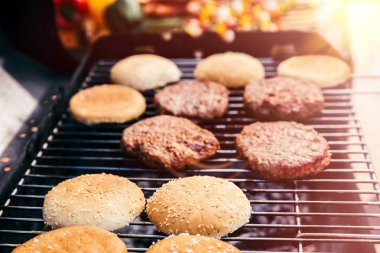 Bread and meat cooked for burgers outdoors on grill clipart