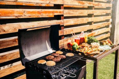 Seasonal vegetables and burgers cooked outdoors on grill clipart