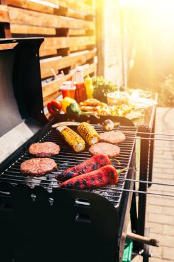 Burger patties and vegetables cooked outdoors on grill clipart