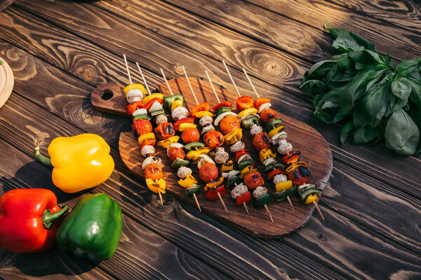 Wooden board with vegetables and mushrooms on skewers cooked outdoors on grill