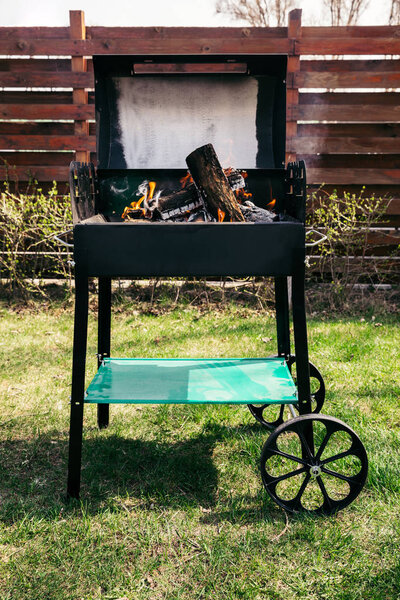 Metal outdoor grill with logs burning on fire