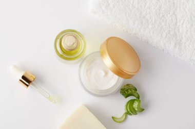 beyaz yüzey üzerinde organik krem, Kozmetik yağı ve sabun, pipet, havlu ve aloe vera dilimleri Üstten Görünüm 
