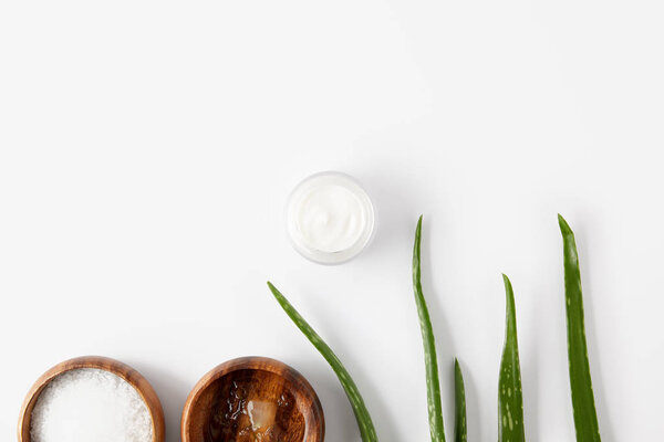elevated view of two wooden bowls with aloe vera juice and salt, organic cream in container and aloe vera leaves 