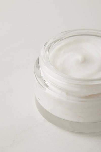 close up view of organic cream in container on white surface