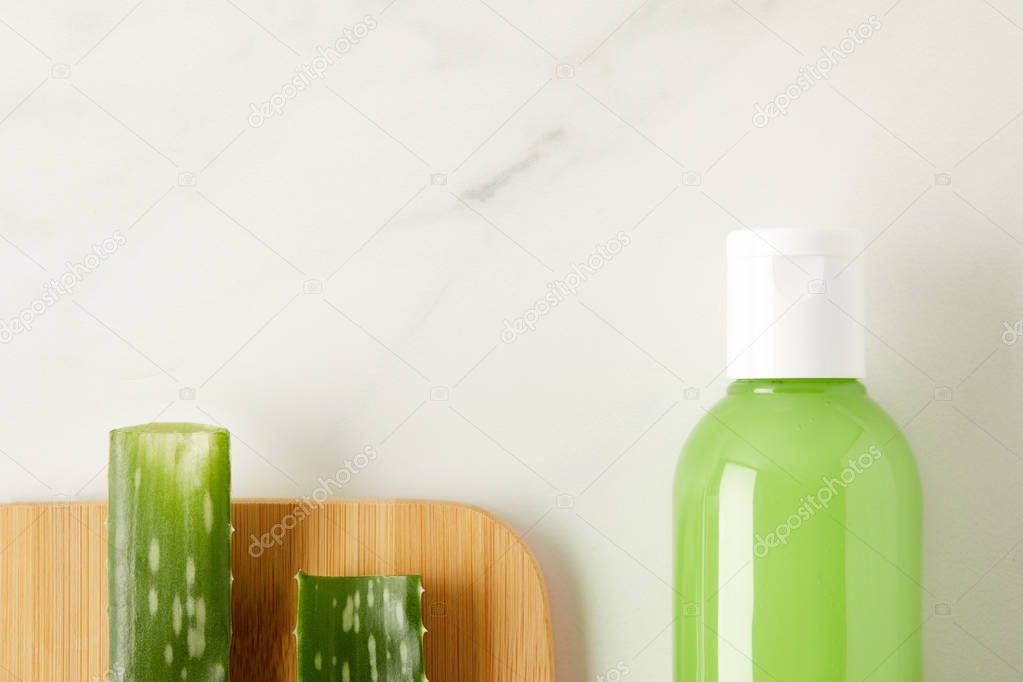 elevated view of aloe vera leaves on cutting board and organic shower gel in bottle on marble table 