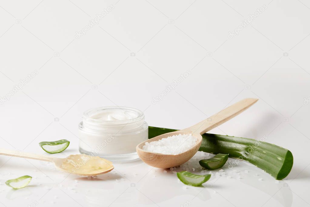organic cream in container, aloe vera leaf and slices and two spoons with salt and juice