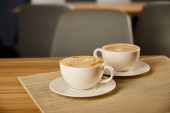 selective focus of creamy cappuccino in white cups on table 