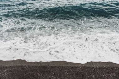 Kıyı şeridindeki kumlu sahilde beyaz köpüklü deniz dalgaları 