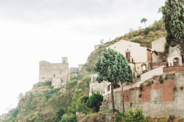 Savoca, İtalya - 3 Ekim 2019: Yeşil ağaçların ve küçük evlerin yanındaki tepede San Nicolo Kilisesi