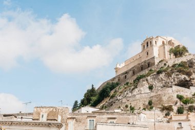 Scicli, İtalya - 3 Ekim 2019: San Matteo Kilisesi 'nin alçak açısı ve İtalya' daki küçük binaların yakınındaki yeşil ağaçlar 