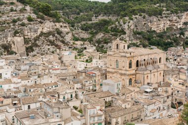 Scicli, İtalya - 3 Ekim 2019: Yeşil ağaçların yanında küçük evleri ve İtalya 'da San Bartolomeo kilisesi olan eski bir şehir 