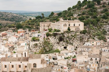 Scicli, İtalya - 3 Ekim 2019: Yeşil ağaçlar ve San Matteo kilisesi yakınında küçük evleri olan İtalyan şehri 
