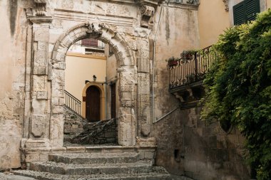 ancient arch in old building near green plants in modica, italy  clipart