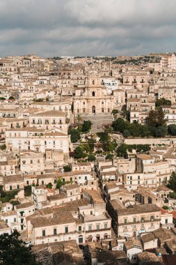 Modica, İtalya - 3 Ekim 2019: evlerin ve yeşil ağaçların yakınlarındaki San Giorgio barok katedrali 