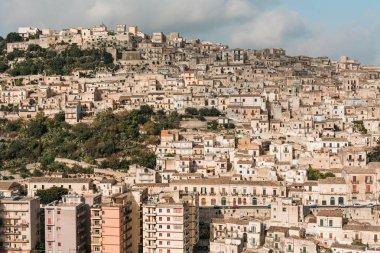 Güneş ışığı yeşil ağaçların yanındaki evlerde gökyüzüne karşı ragusa, İtalya 'da bulutlarla 