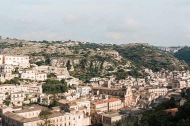 Güneş ışığı yeşil ağaçların yanındaki küçük evlerde gökyüzüne karşı ragusa, İtalya 'da bulutlarla 