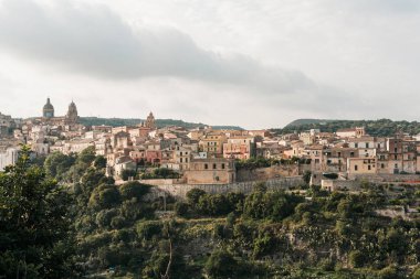 Ragusa, İtalya 'da bulutlu küçük evlerin yanındaki yeşil ağaçlar gökyüzüne karşı. 