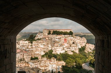 arch near small houses and green trees in ragusa, italy  clipart