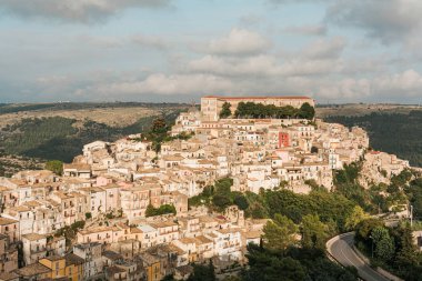 sunlight on small houses and green trees on hill in ragusa, italy  clipart