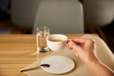 Kafede bir bardak suyun yanında elinde kahve tutan bir kadın görüntüsü. 
