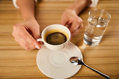 selective focus of woman holding cup of coffee near glass of water in cafe  clipart